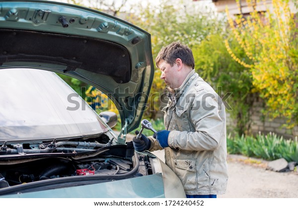 Dnipro, Ukraine, April 24, 2020. An Asian\
technician measures the battery voltage in a car at a service\
station, maintenance and repair. Car repair on the street near the\
house. Hands of a man\
repairi