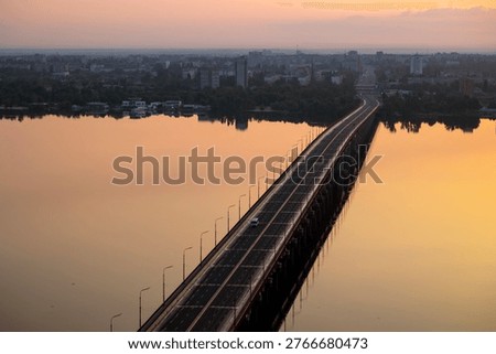 Dnipro, Ukraine, an elevated view of a long city bridge spanning the wide river at dawn on may 19, 2023, showcasing the serene water reflecting the warm sky and the distant urban skyline