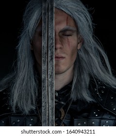 Dnipro, Ukraine - February 06, 2020: Portrait Of Cosplayer In Image Of Character Geralt Of Rivia From The Game Or Film The Witcher With Sword In His Arms.