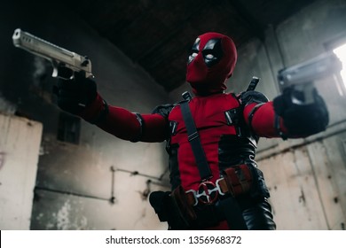 DNIPRO, UKRAINE - MARCH 28, 2019: Deadpool cosplayer posing indoors with two guns in his hands and katanas behind his back.