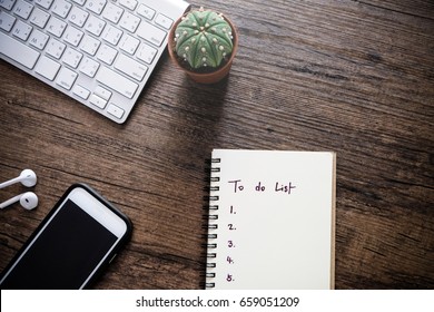 To Do List By Priority In Note Book Beside Are Smart Phone,keyboard,cactus And Small Talk On Wooden Table, Business Concept