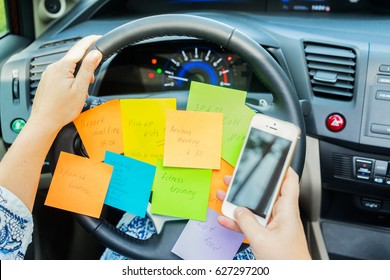 To do list in a car on driving wheel and hand holding phone - busy day concept