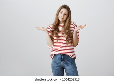 I do not care about rules. Portrait of indifferent careless teenage girl with blonde hair shrugging and holding spread palms near shoulders, being uninterested and bothered with stupid questions