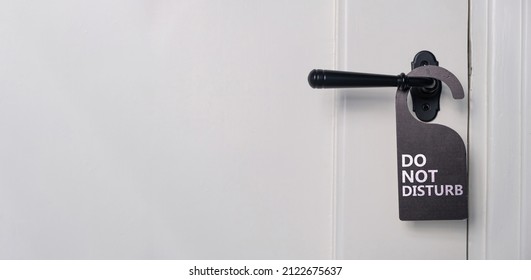 Do not disturb text sign, hotel room hanger. Black label on closed retro paneled door handle, close up view. White wooden doorway