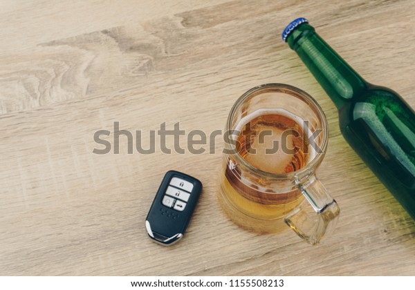 do not drink and drive concept, close up of a mug\
of beer and a beer bottle with a remote car key on wooden table,\
selective focus