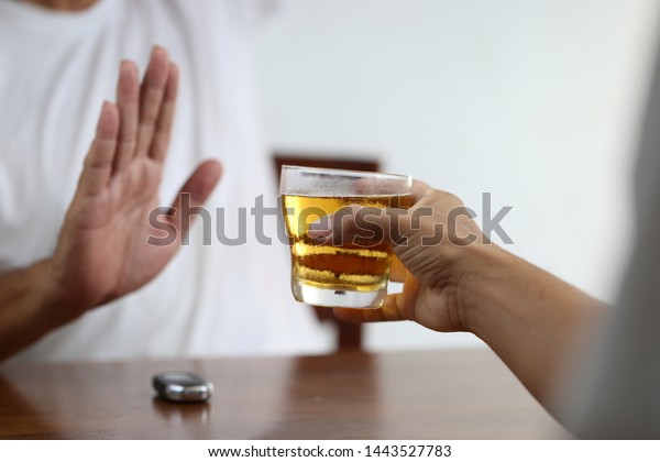 Do not drink and drive concept, Man hand\
holding glasses of beer and Man showing stop gesture and refusing\
to drink beer with car keys on the\
table