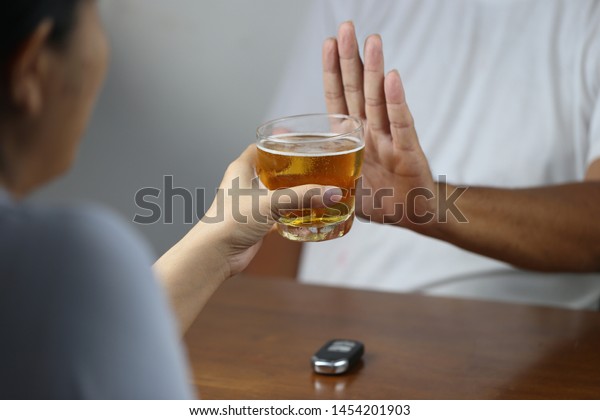 Do not drink and drive concept,\
Young woman hand holding glasses of beer and Man showing stop\
gesture and refusing to drink beer with car keys on the\
table