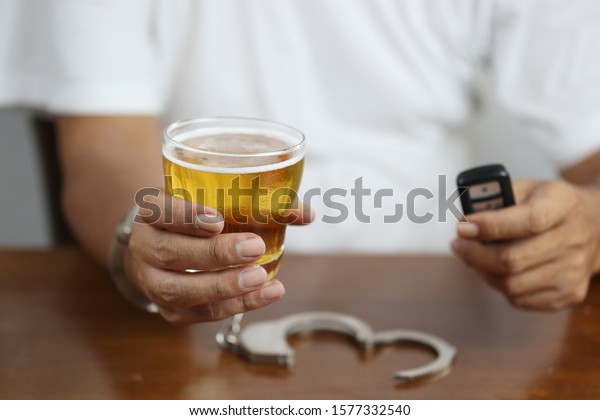 Do not drink and\
drive concept, Man hand holding glasses of beer with car keys and\
shackle on the table in bar