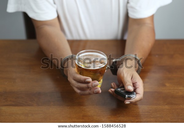 Do not drink and\
drive concept, Man hand holding glasses of beer with car keys and\
shackle on the table in bar