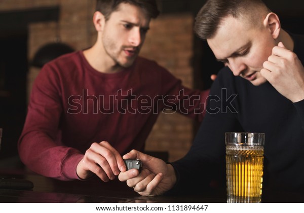Do not drink and drive.\
Depressed drunk man taking car keys and his friend stopping him,\
copy space
