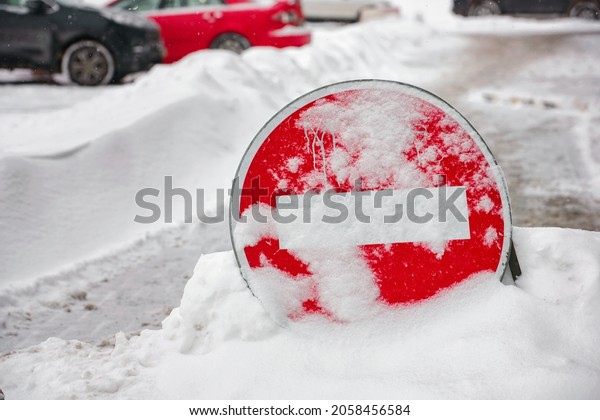 Do not enter road\
sign. Car traffic prohibited. Warning no entry zone. Drive in\
forbidden. No entry - road sign during snowfall, covered with snow,\
parked cars on background