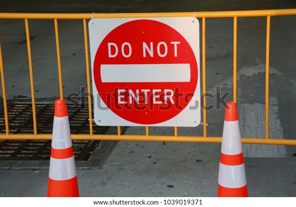 Do Not Enter Sign on Metal Railing\
Flanked by Two Cones in Front of Parking Garage at\
Dusk