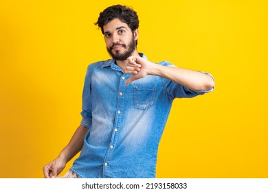 I Do Not Have More Money. Portrait Of Sad Bankrupt Bearded Young Man In Blue Casual Style Shirt Standing And Showing Empty Pocket And Looking At Camera. Indoor Studio Shot, Isolated On Yellow 