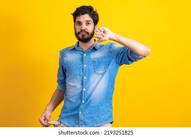 I Do Not Have More Money. Portrait Of Sad Bankrupt Bearded Young Man In Blue Casual Style Shirt Standing And Showing Empty Pocket And Looking At Camera. Indoor Studio Shot, Isolated On Yellow 