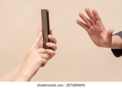 Do Not Shoot Concept. No Photo. One Person With Smartphone Photo Camera In Hand And Stop Gesture By Another Hand Close Up. Personal Space.