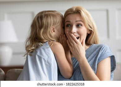 Do Not Tell Anyone. Cute Little Kid Daughter Sharing Secrets With Trusted Millennial Mother, Naughty Preschool Girl Whispering Funny Gossip Or Joke On Ear Of Amazed Shocked Laughing Grown Elder Sister