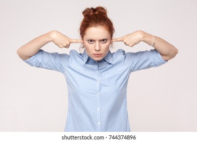 I do not want to hear from you! Aggressive ginger woman holding fingers on ears and looking at camera. Studio shot