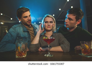 I Do Not Want To Tell About It. Portrait Of Disappointed Female Talking With Two Interested Guys. Acquaintance With Men In Club Concept