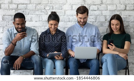 Do not waste time in queue, spend it online. Focused concentrated diverse young people applicants sitting in line expecting for job interview using different gadgets reviewing information checking cv