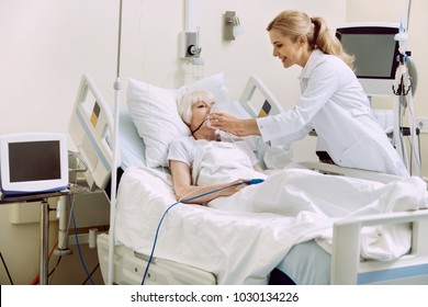 DO Not Worry. Friendly Female Medical Worker Smiling While Helping Her Retired Patient And Adjusting An Oxygen Mask At Hospital.