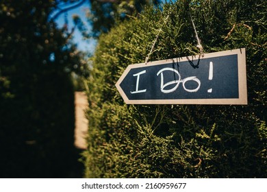 I Do written on a blackboard sign hanging on a bush at a country wedding - Shutterstock ID 2160959677