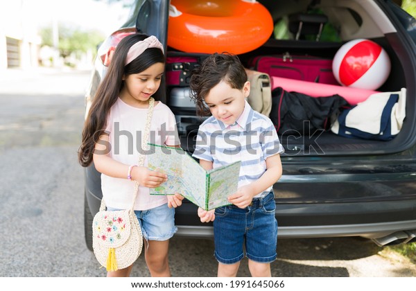 Do you know where we are going? Beautiful little\
siblings looking at a road map while waiting for mom and dad in the\
car for a family trip