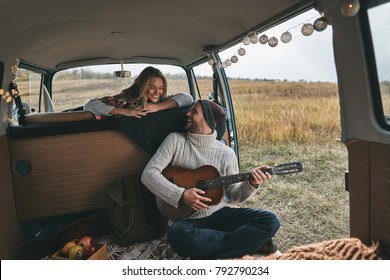 Do You Like My New Song?  Handsome Young Man Playing Guitar For His Beautiful Girlfriend While Sitting In Retro Style Mini Van