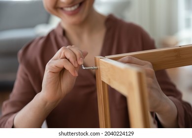 Do it yourself. Close up shot of smiling young female assembling flat pack furniture at home using hex key. Satisfied woman customer screw details of wooden shelf together with allen key by own hands