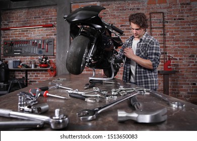 Do It Yourself, Young Man Repairing A Motorcycle In The Garage With Red Brick Wall, Pegboard Work Tools And Wrenches On The Work Bench, Concept Of Ability And Success