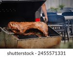 Dobele, Latvia - August 18, 2023 - A whole pig being roasted on a large barbecue grill with a person standing behind.