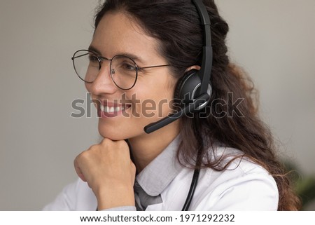 Doc speaking. Friendly young hispanic woman medical consultant gp wear glasses modern wireless headphones take patients calls. Smiling female doctor healthcare helpline worker ready to assist online