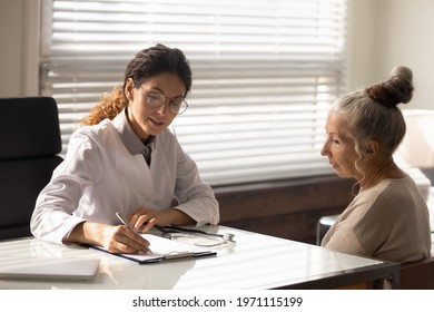 Doc at work. Focused doctor in glasses write diagnosis symptoms of mature woman patient in medical case. Female family therapist interview sick elderly lady take notes fill in paper declaration form - Powered by Shutterstock