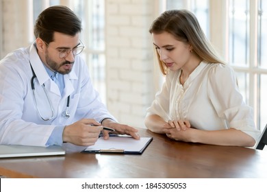 Doc writing prescription. Capable qualified millennial male doctor attending physician gynecologist gp consulting young female patient at hospital cabinet, ordering medication, prescribing treatment - Powered by Shutterstock