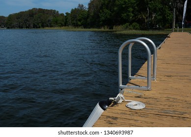 A dock at a lake with a ladder and a cleat tied with a dock line which looks inviting  for a swim.