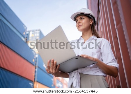 Dock manager or engineer worker in causual suit standing in shipping container yard holding laptop with smile. Import and export product. Manufacturing transportation and global business concept.