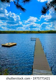 Dock And Raft On The Shoreline Of A Lake In Northern Wisconsin.  Clouds Overhead With The Sun Shining Through.