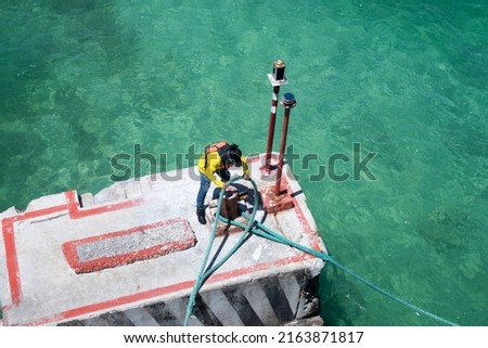 A dock worker pulls ropes a ship , wrapped around a mooring bollard on a dock in the harbor.