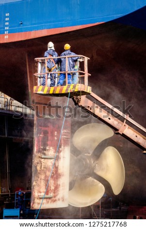 Dock workers at work on a vessel hull in a ship repair drydock.