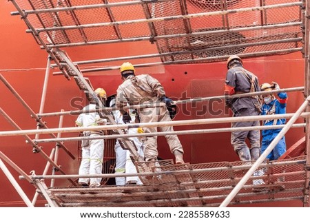 Dock yard, shipyard employees are working near the big container vessel hull. She is inside drydock for scheduled repairs and painting.   
