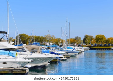 Docked yachts, boats, sailboats, motorboats and calm water in marina against bright blue sky and autumn trees background. Picturesque urban landscape photo. - Powered by Shutterstock