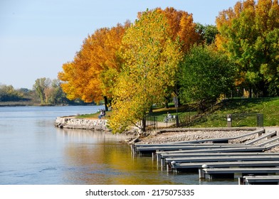 Docks Line The Fox River Shoreline At Vpyageur Park In De Pere, Wisconsin.  People Enjoy The Park In The Background.