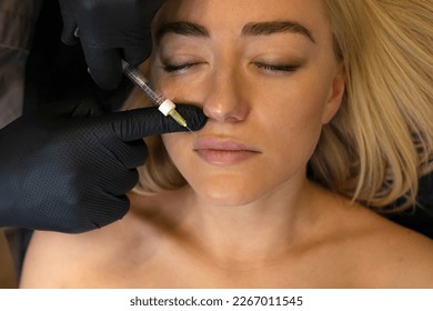 Doctor adds volume to woman's lips with lip filler, injection. White female lying on couch. Beauty physician holds syringe near girl's face.Lip augmentation procedure.Cosmetologist,aesthetic medicine