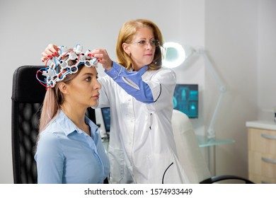 Doctor Adjusting Neurology Helmet During A Brain Scan Procedure. Woman Patient