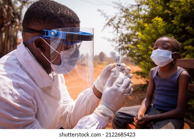 Doctor Adjusts The Syringe To Inject The Vaccine To An African Child. Concept Of Covid-19 Vaccination In Africa. Coronavirus Vaccine.