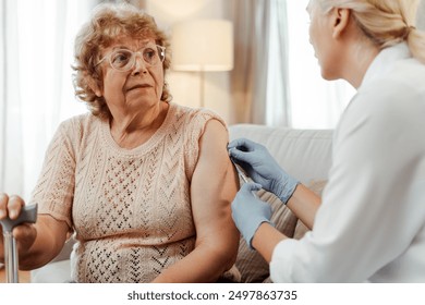 Doctor administers a vaccine to a senior woman at home, emphasizing virus prevention and healthcare for the elderly. Immunization concept - Powered by Shutterstock