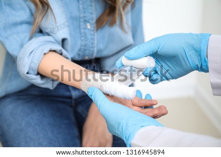 Doctor applying bandage onto finger of young woman, closeup