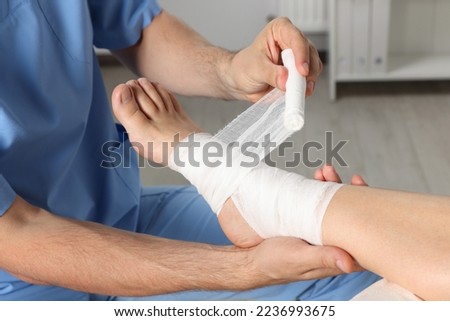 Doctor applying bandage onto patient's foot in hospital, closeup