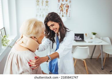 Doctor Applying Cervical Collar On Neck Of Senior Woman In Clinic. Female Doctor Putting Neck Orthopaedic Collar On Adult Injured Woman. Woman In Pain At The Doctor For A Neck Injury