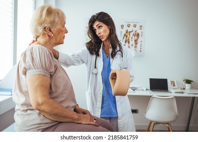 Doctor Applying Cervical Collar On Neck Of Senior Woman In Clinic. Female Doctor Putting Neck Orthopaedic Collar On Adult Injured Woman. Woman In Pain At The Doctor For A Neck Injury