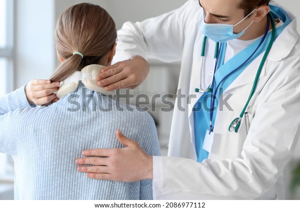 Doctor applying cervical collar on neck of young\
woman in clinic